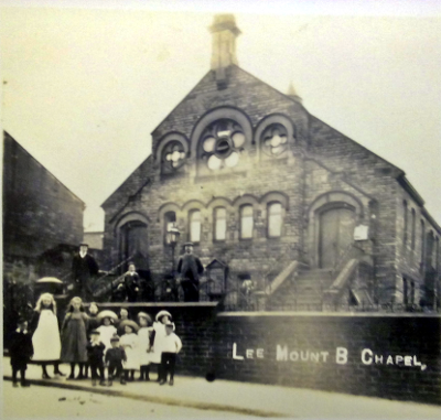 View of the school-chapel from the road with a group of children on the pavement in front of the wall and three adults in the grounds in front of the chapel